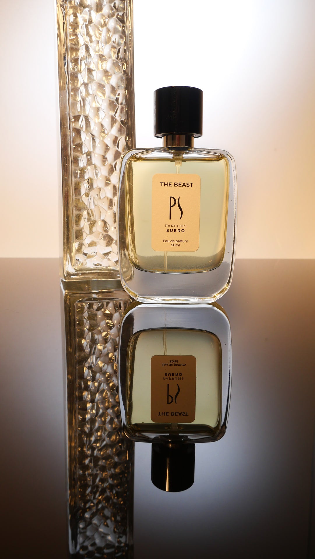 le flacon du parfum the beast de la marque parfums suero sur un miroir noir a coté d'une pièce de verre pressé