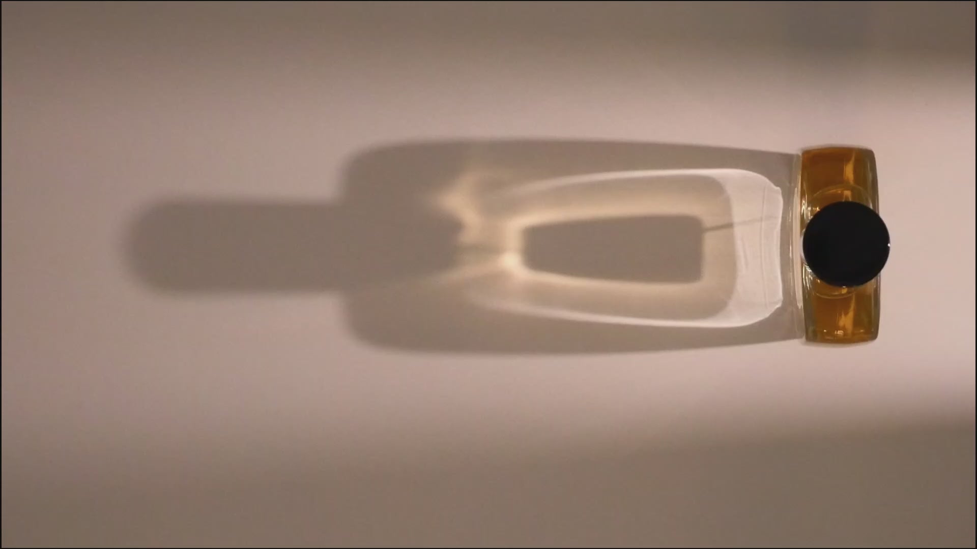 un flacon de la marque PARFUMS SUERO entre dans un faisceau lumineux progressif faisant apparaitre son ombre projetée