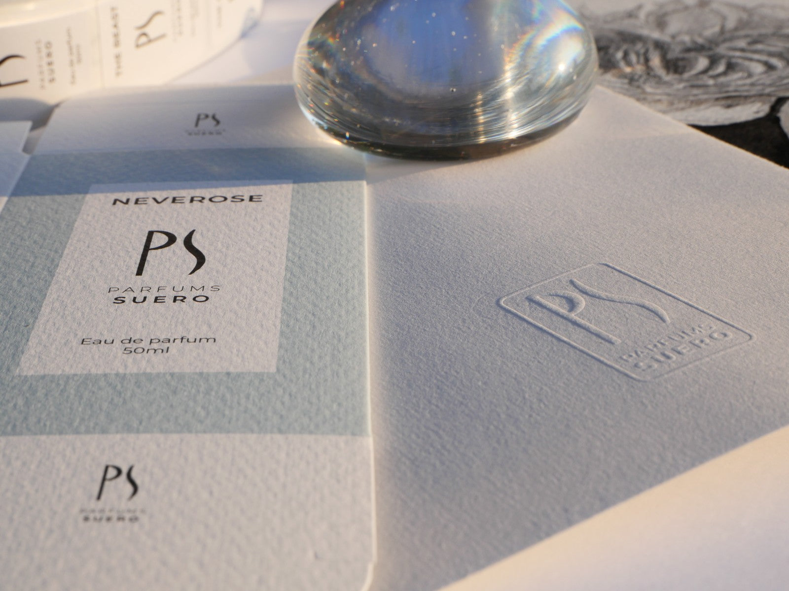 la photo montre un détail du bureau du créateur de la marque PARFUMS SUERO où l'on voit le logo embaussé et une boite pliée